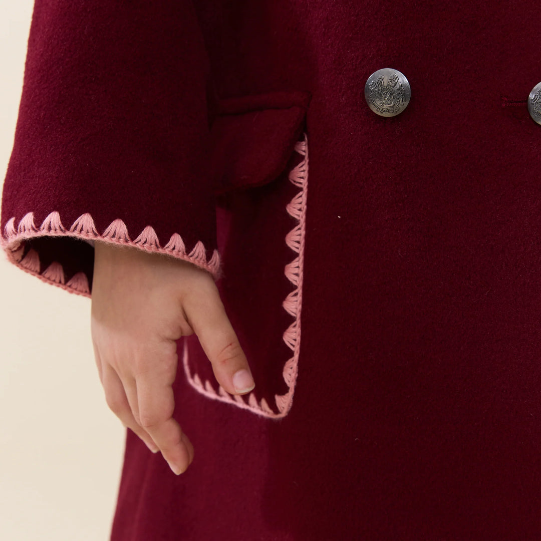 Close-up of Girls Beck Peacoat Burgundy showing pink embroidered trim, pocket, and decorative metal buttons