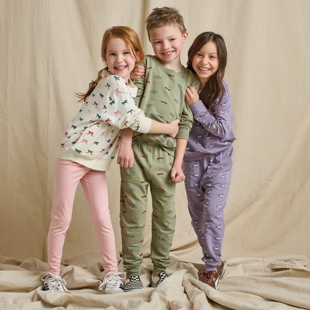 Girl wearing a cream bow print sweatshirt with pink leggings alongside children in coordinating printed outfits
