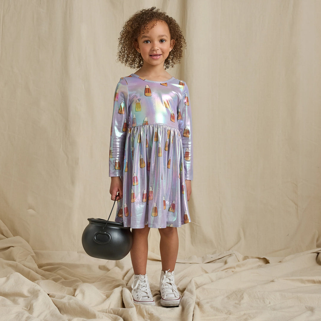 Girl wearing an iridescent lavender candy corn Halloween dress with long sleeves and a gathered skirt while holding a black trick-or-treat cauldron.