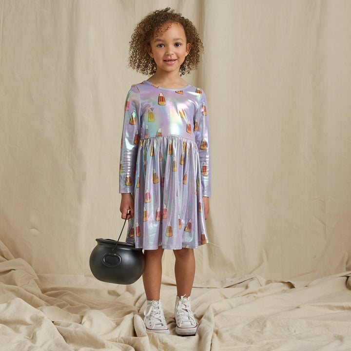 Girl wearing an iridescent lavender candy corn Halloween dress with long sleeves and a gathered skirt while holding a black trick-or-treat cauldron.