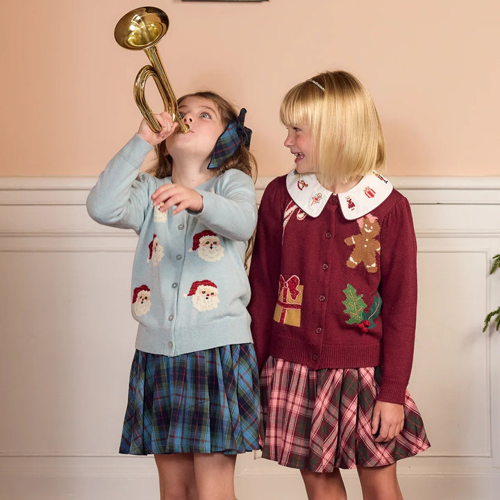 Girl wearing Pink Chicken Girls Constance Sweater Tossed Santas with a blue tartan skirt while playing a toy trumpet