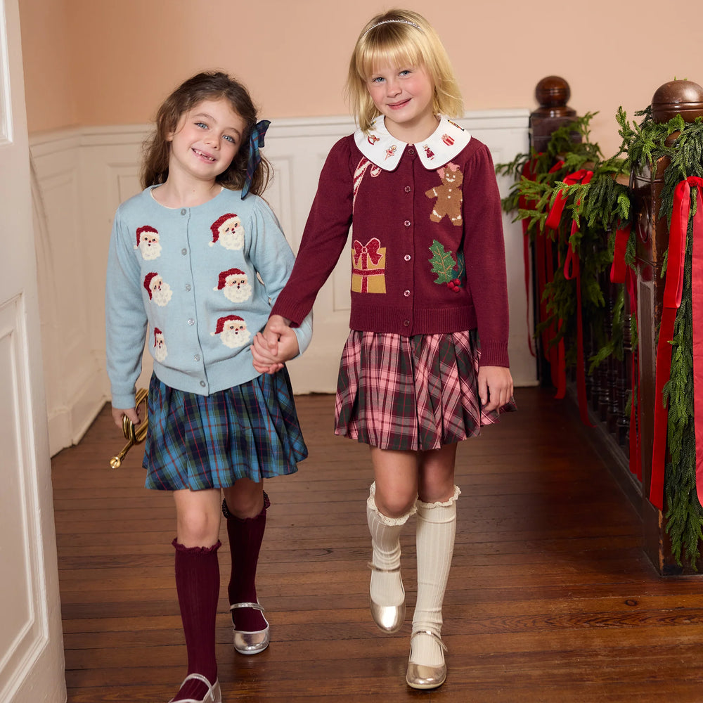 Girl wearing the light blue Tossed Santas Constance Sweater with a blue plaid skirt for a festive Christmas outfit