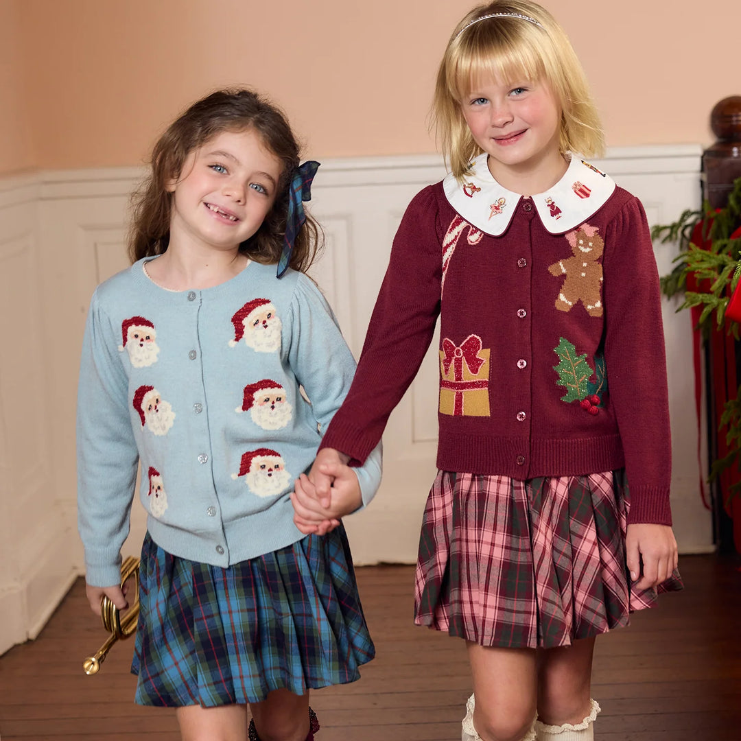 Young girl wearing the Pink Chicken Burgundy Tartan Gianna Skirt with a burgundy Christmas cardigan featuring festive gingerbread and holiday designs.