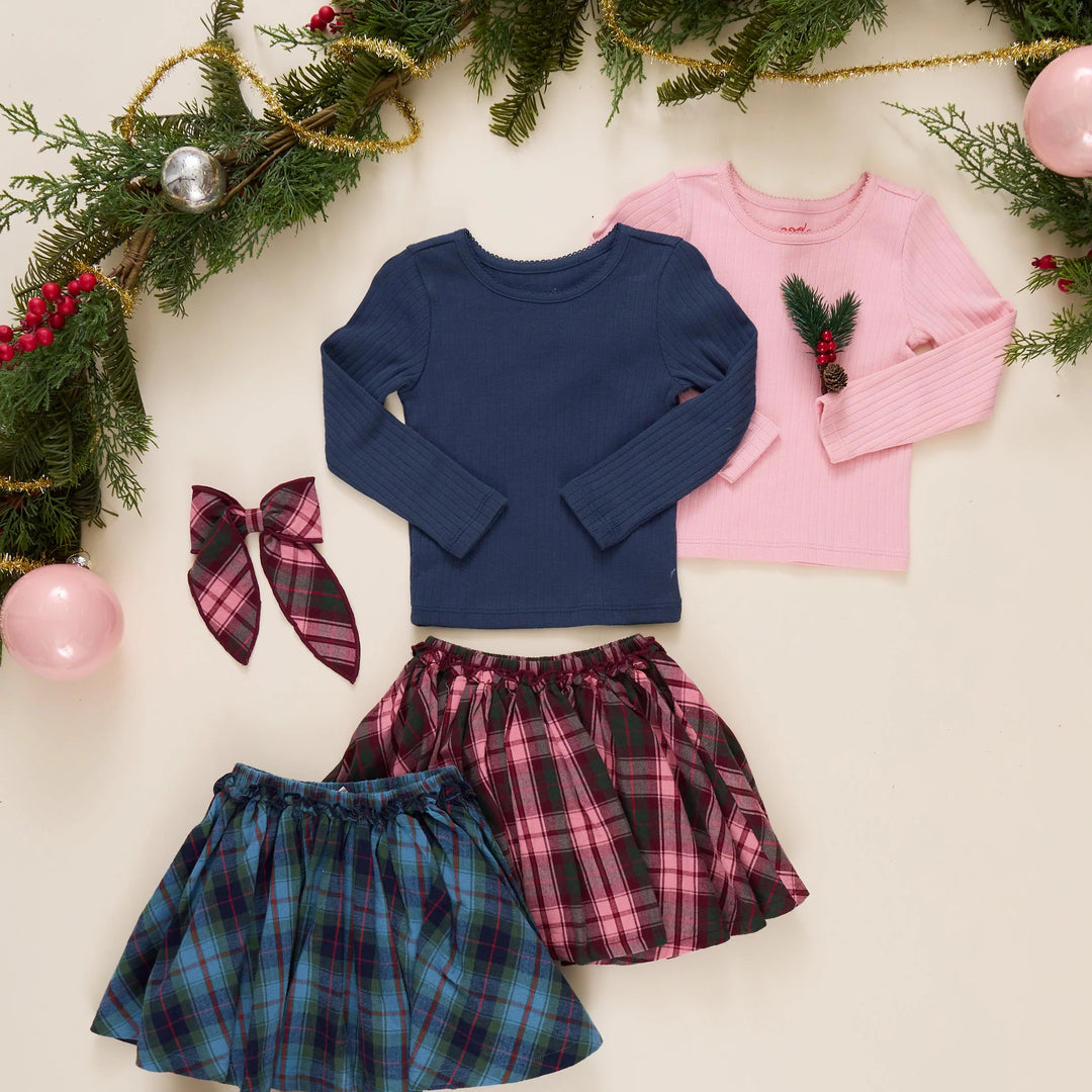 Pink Chicken Burgundy Tartan Gianna Skirt styled in a holiday flat lay with coordinating blue and pink tops, plaid accessories, and Christmas greenery.