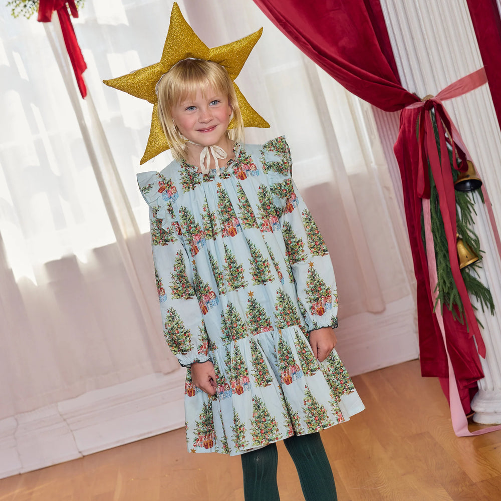 Young girl modeling the Pink Chicken Girls Harper Dress in Trees and Presents with green tights and a gold star headpiece for Christmas.