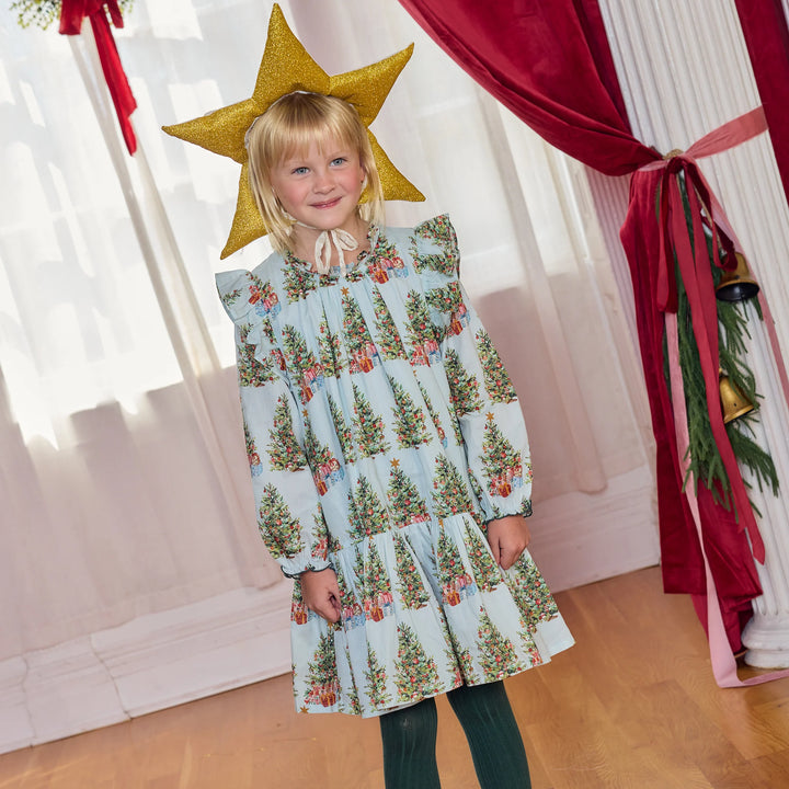 Young girl modeling the Pink Chicken Girls Harper Dress in Trees and Presents with green tights and a gold star headpiece for Christmas.