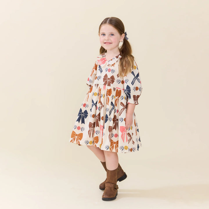 Girl wearing cream Girls Harvest Bow Dress with boots for a sweet autumn look