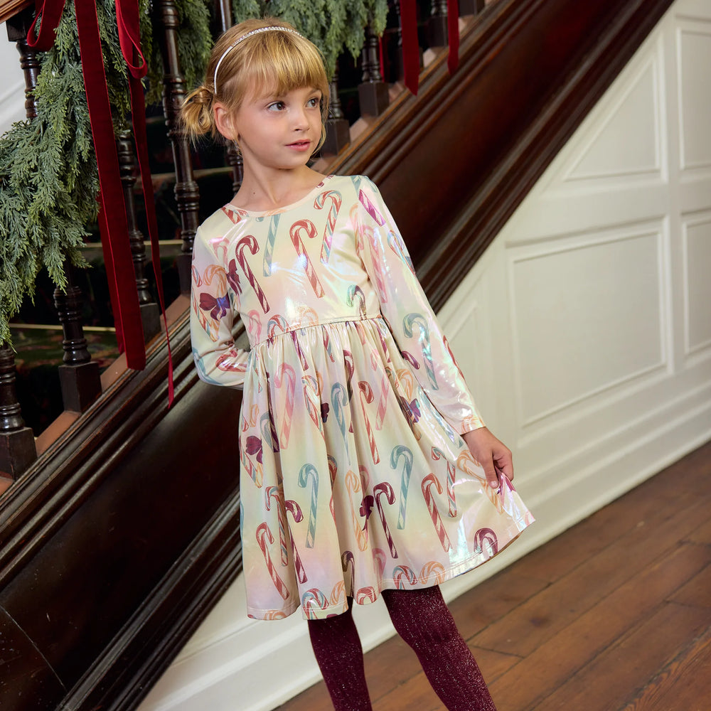 Young girl wearing the Pink Chicken Girls Lame Steph Dress in Antique Candy Canes with burgundy glitter tights beside a Christmas-decorated staircase.