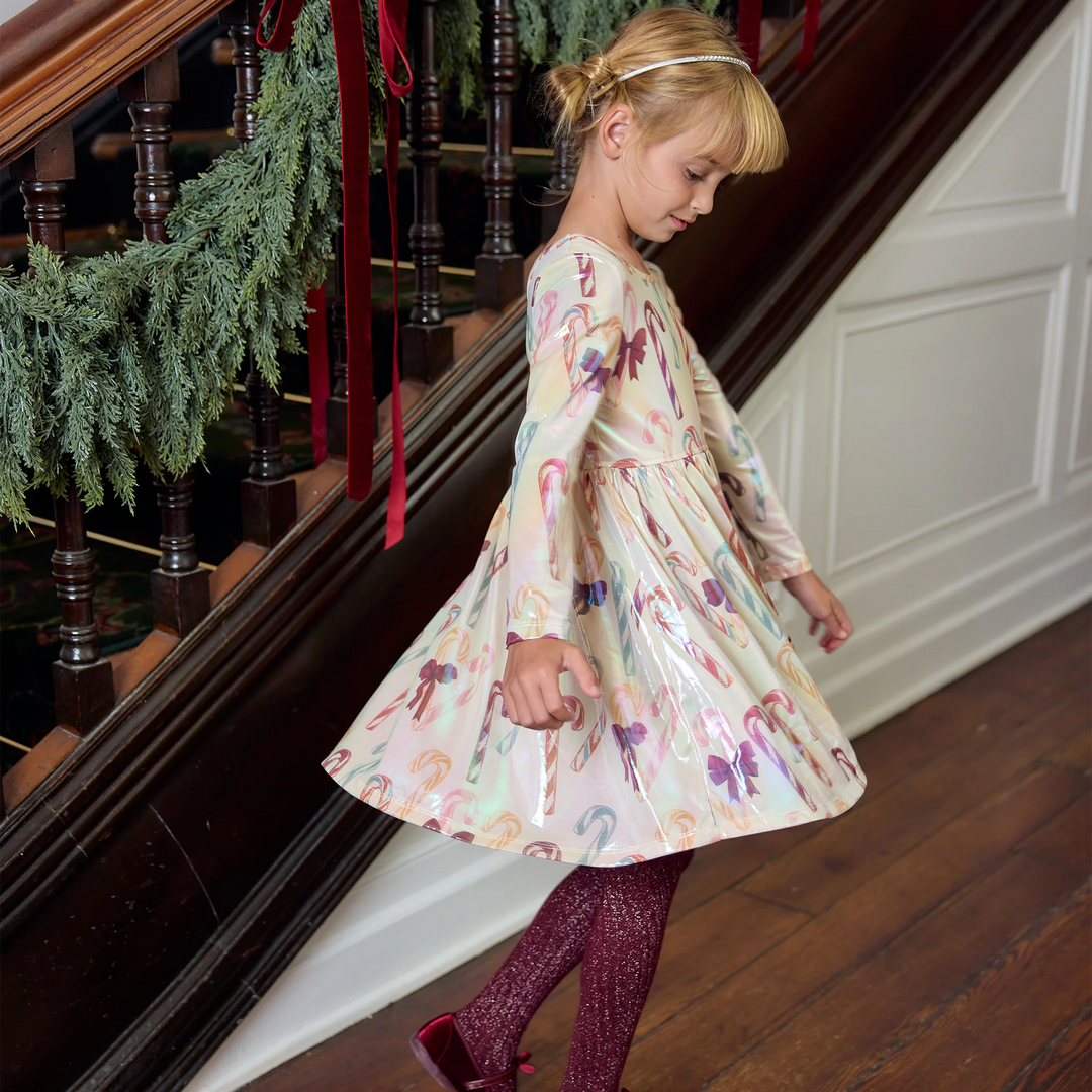 Girl twirling in the Pink Chicken Girls Lame Steph Dress, showcasing its shimmering candy cane print, long sleeves, and full gathered skirt.