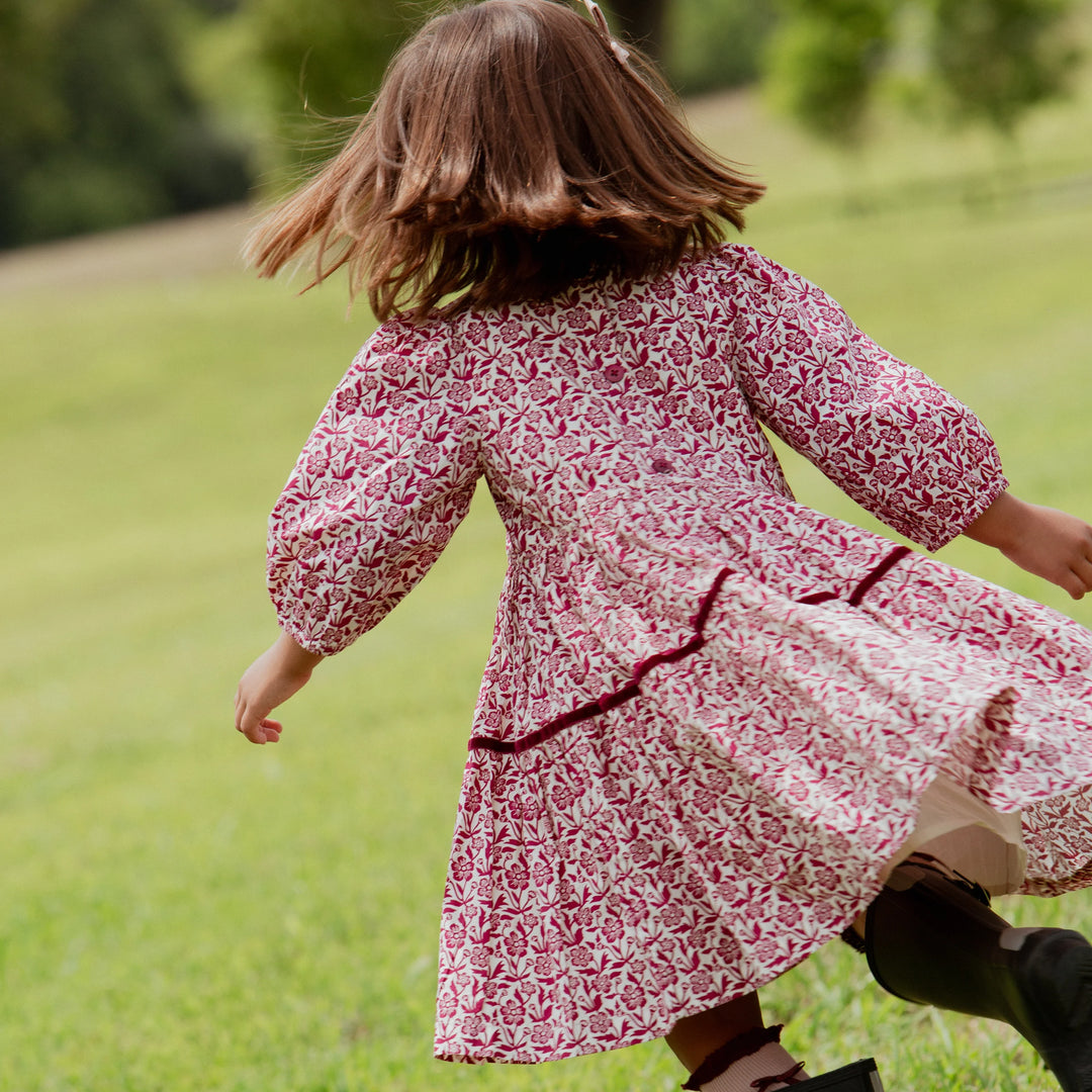Girl twirling in the Girls Maribelle Dress featuring a burgundy floral print and tiered skirt