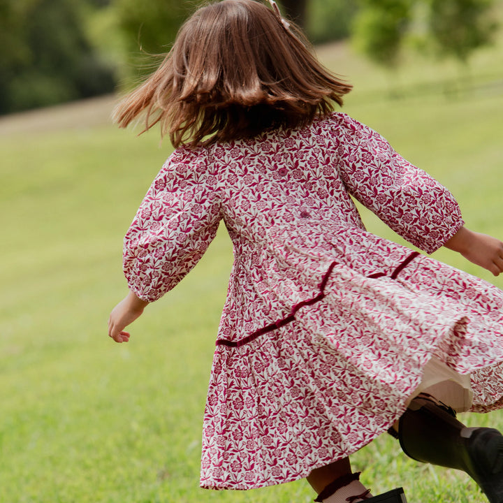 Girl twirling in the Girls Maribelle Dress featuring a burgundy floral print and tiered skirt