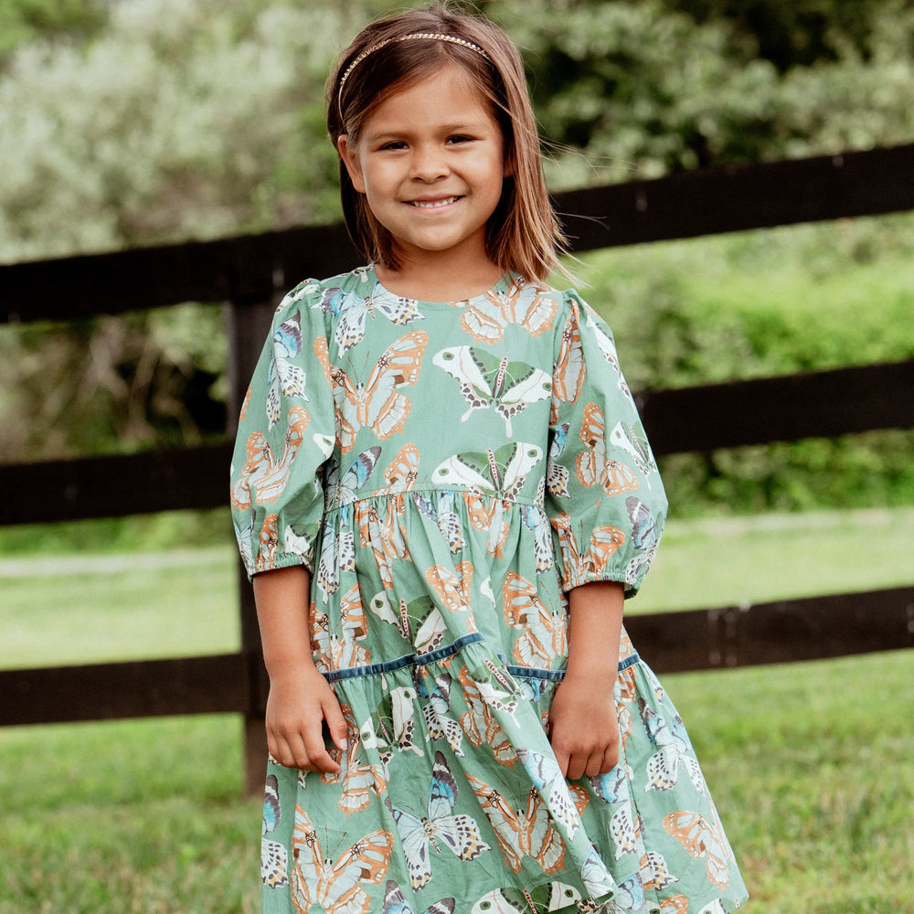 Girl wearing Girls Maribelle Dress Green Butterflies with colorful butterfly print and puff sleeves