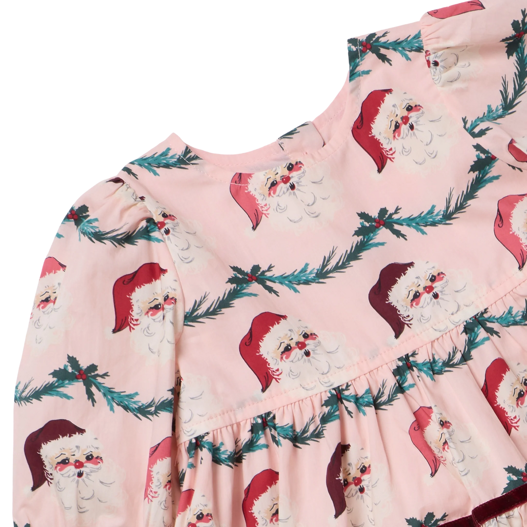 Close-up of the Girls Maribelle Dress in Santa Garland showing vintage Santa faces, evergreen garland print, gathered puff sleeves, and pink fabric.