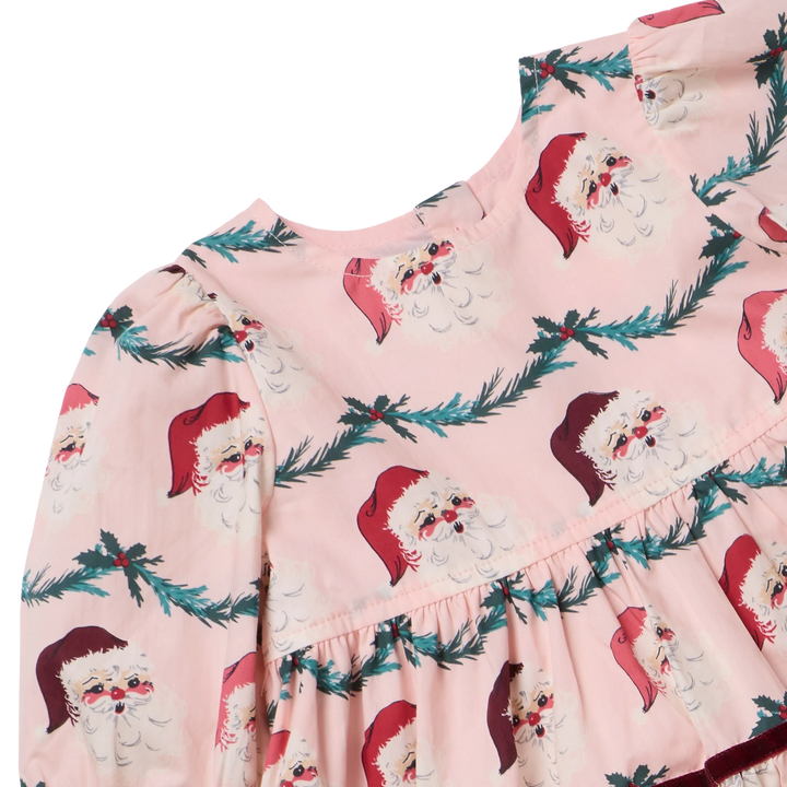 Close-up of the Girls Maribelle Dress in Santa Garland showing vintage Santa faces, evergreen garland print, gathered puff sleeves, and pink fabric.