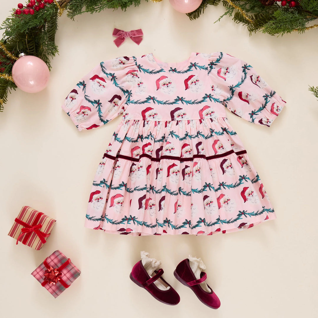 Pink Chicken Girls Maribelle Dress in Santa Garland styled with burgundy velvet shoes, Christmas presents, and festive greenery.