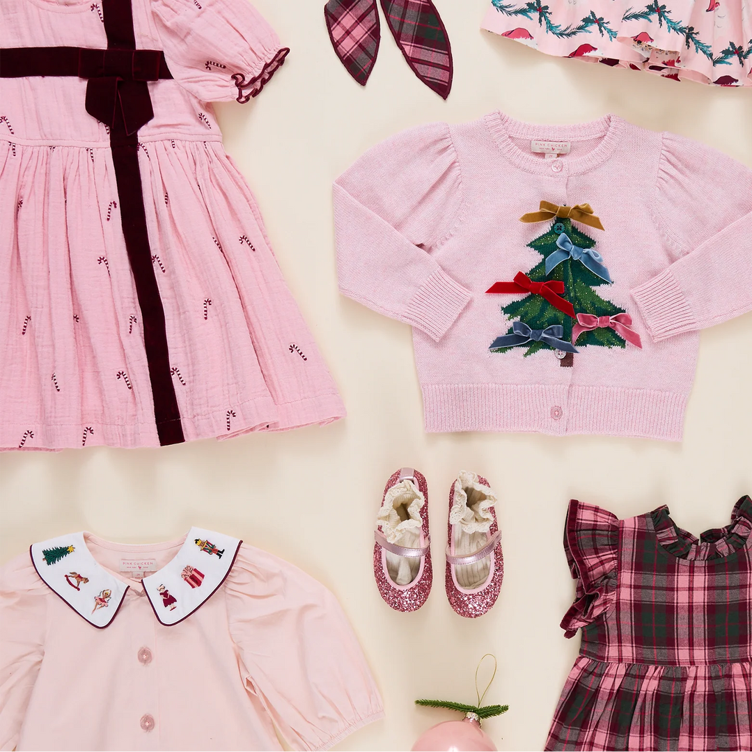 Pink Chicken Girls Noelle Top displayed in a festive holiday flat lay alongside pink Christmas dresses, a Christmas tree cardigan, and glittery pink shoes.