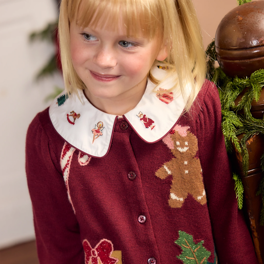 Young girl wearing the Nutcracker embroidered collar of the Pink Chicken Noelle Top layered over a burgundy Christmas cardigan.