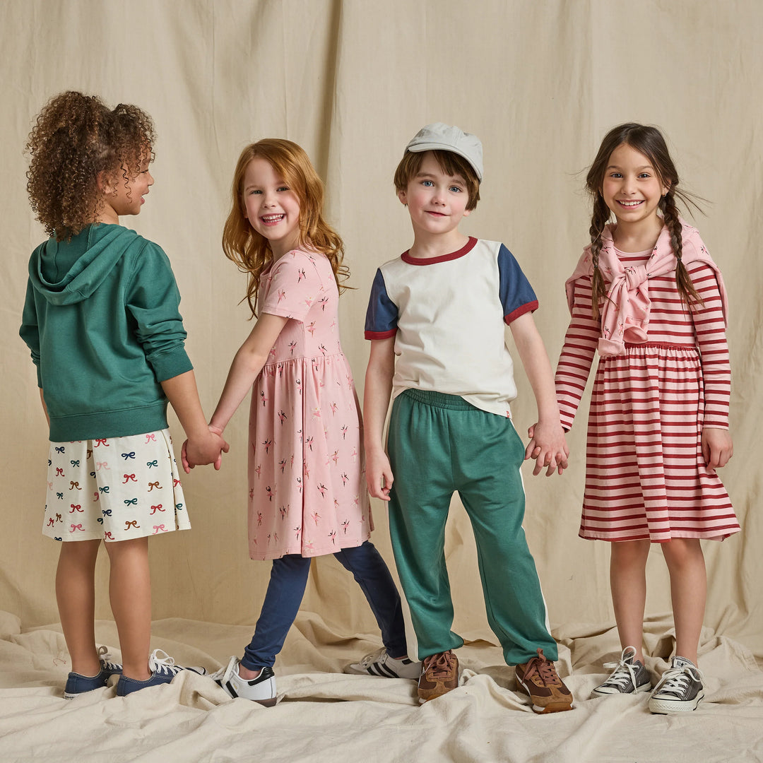 Girl wearing a pink and red striped long sleeve dress styled with sneakers in a kids fall clothing lifestyle image.