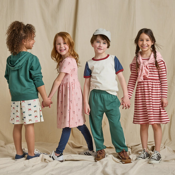 Girl wearing a pink and red striped long sleeve dress styled with sneakers in a kids fall clothing lifestyle image.