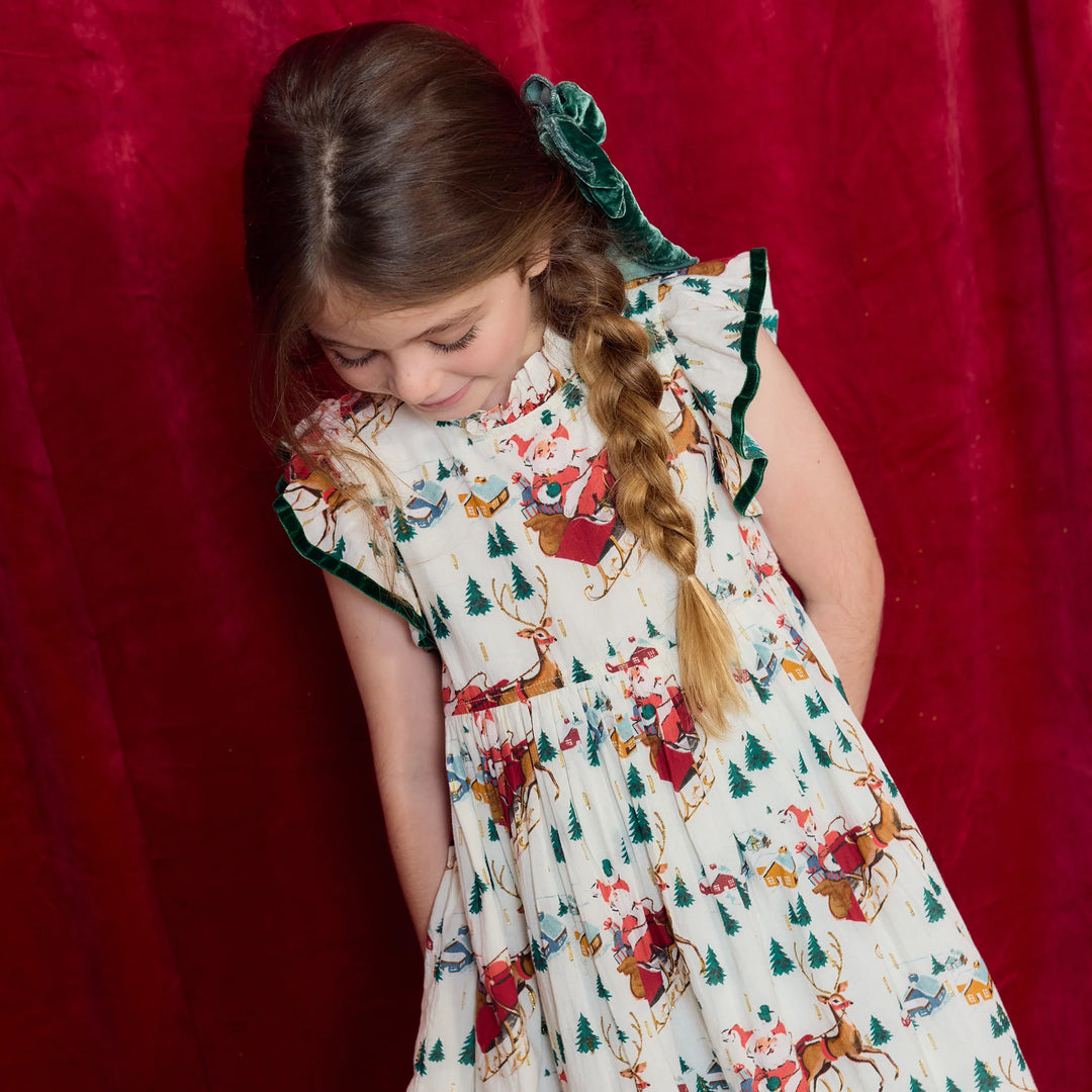 Close-up of girl wearing Santa Sleigh Christmas Dress featuring flutter sleeves, green velvet trim, and holiday print