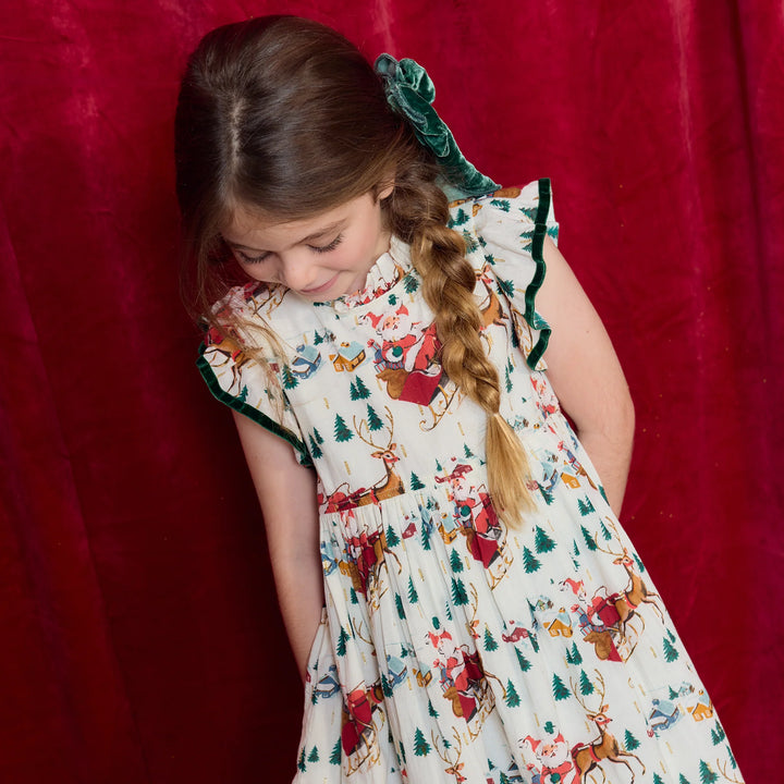 Close-up of girl wearing Santa Sleigh Christmas Dress featuring flutter sleeves, green velvet trim, and holiday print