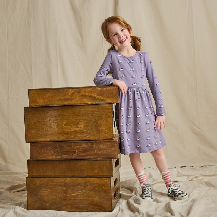 Girl wearing a lavender long sleeve unicorn dress with colorful horse print and gathered skirt