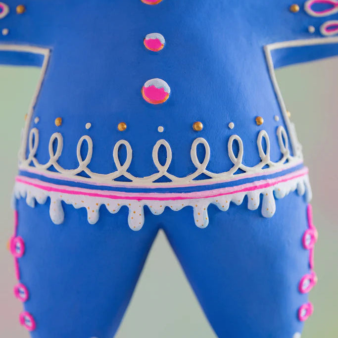 Close-up of the Glitterville Blue Dough gingerbread figure showcasing intricate hand-iced details, including pink and white candy buttons, looping white icing, gold sugar accents, pink trim, dripping white icing, and decorative pink icing along the legs. A detailed view of the whimsical blue Glitterville gingerbread Christmas collectible.