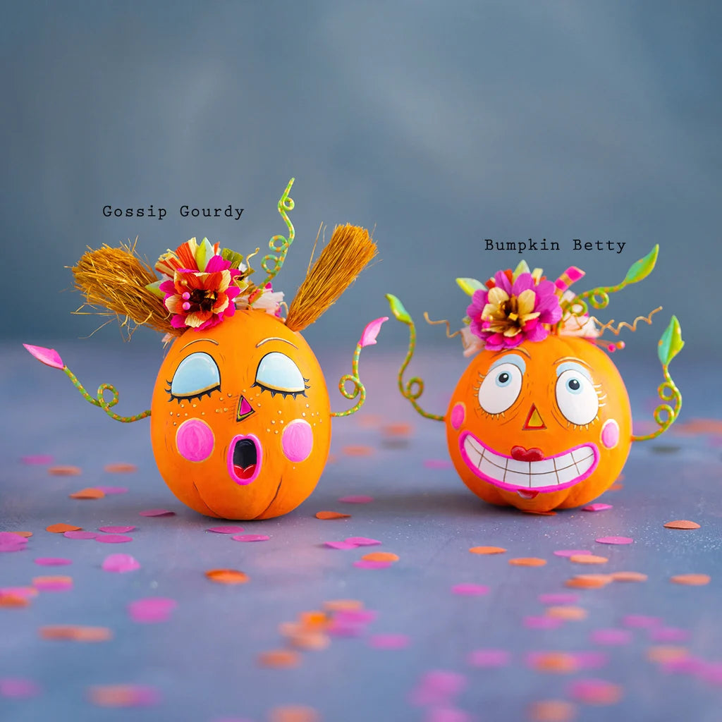 Glitterville Bumpkin Betty and Gossip Gourdy pumpkin tabletop figurines featuring playful faces, colorful floral accents, and whimsical Halloween details. Names are labeled above each pumpkin for easy distinguishing. 