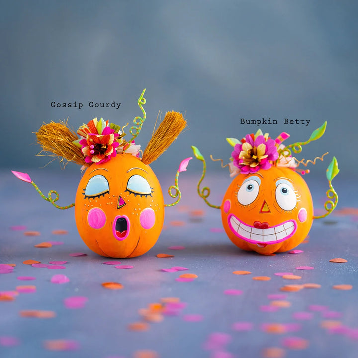 Glitterville Bumpkin Betty and Gossip Gourdy pumpkin tabletop figurines featuring playful faces, colorful floral accents, and whimsical Halloween details. Names are labeled above each pumpkin for easy distinguishing. 