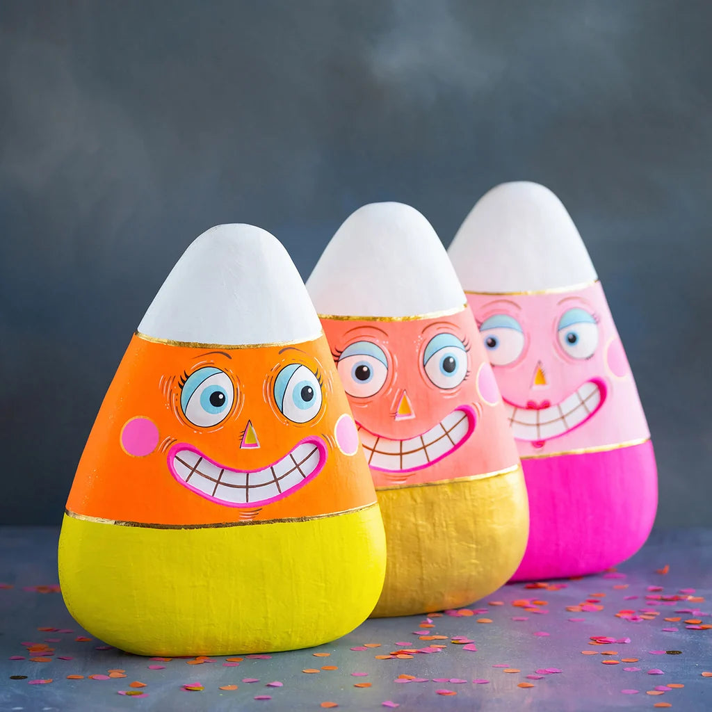 Glitterville Candice, Kettle and Carl candy corn figurines featuring colorful pink, orange, yellow, and white designs with playful smiling faces. Layered one in front of the other, each product compliments the other.