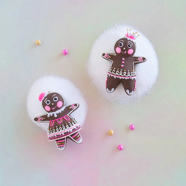 Glitterville Dippsy and Dough gingerbread Christmas ornaments displayed together on a soft snowy background, featuring brown gingerbread figures with intricate pink and white icing, gold accents, decorative details, and Dippsy&