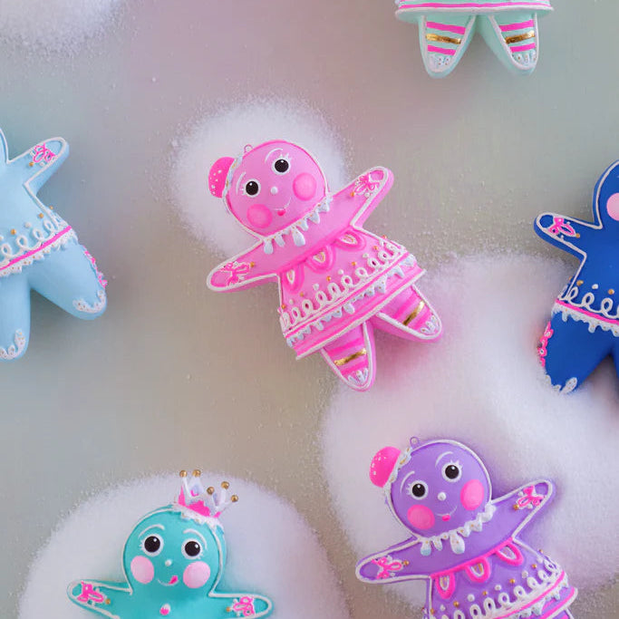 Close-up of several Glitterville Dippsy and Dough gingerbread figure ornaments in pink, light blue, teal, violet, and blue, showcasing their detailed white and pink icing, gold accents, striped legs, rosy cheeks, and whimsical gumdrop and crown headpieces.