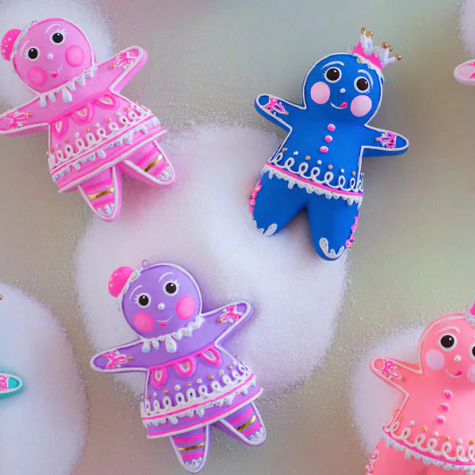 Close-up of several Glitterville Dippsy and Dough gingerbread figure ornaments in pink, blue, violet, and coral, featuring detailed white and pink icing, rosy cheeks, whimsical expressions, and decorative gumdrop and crown headpieces.