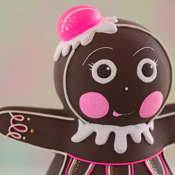 Glitterville Dippsy gingerbread figure head close-up featuring her sweet pink cheeks, expressive white and black icing eyes, delicate white icing eyebrows and smile, scalloped white icing collar, pink decorative accents, and bright pink gumdrop-style hat with white icing and gold sprinkle details.