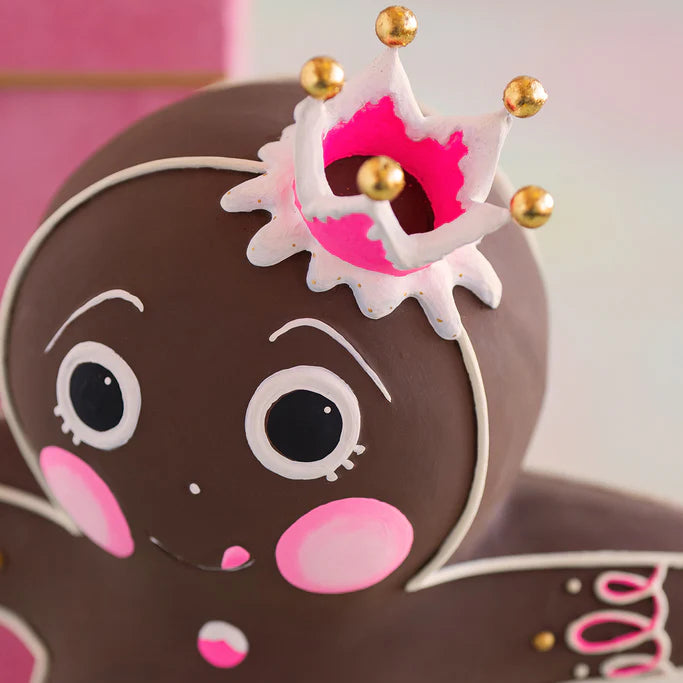 Glitterville Dough gingerbread figure close-up featuring his pink and white icing crown with gold ball accents, expressive white and black icing eyes, pink cheeks, smiling face, and detailed white and pink icing decorations on his brown gingerbread design.
