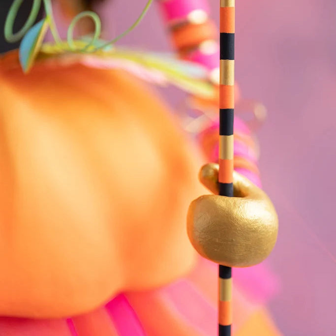 Glitterville Fairy Gourdmother large display close-up showing the gold hand holding her black, orange, and gold striped wand against a pink background.