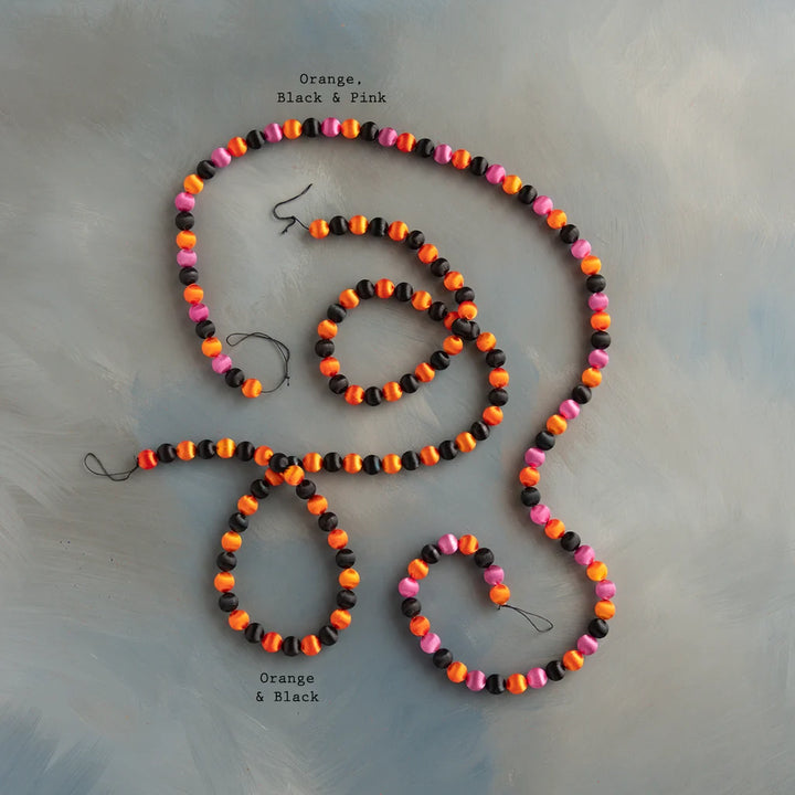 Glitterville Halloween silk ball garland set featuring colorful orange, black, and hot pink silk balls arranged in a festive strand, perfect for Halloween tree decorating, mantels, shelves, party backdrops, and playful seasonal displays. Color combination label displayed near each garland for easy distinguishing. 
