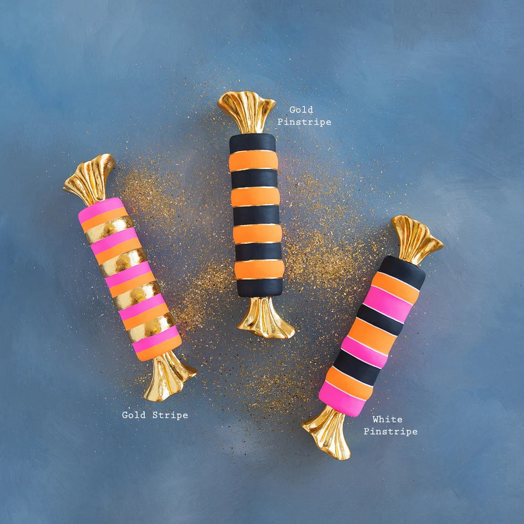 Glitterville Halloween taffy display set featuring three whimsical oversized wrapped candies in black, orange, hot pink, and metallic gold stripes with shimmering gold twisted ends. Stripe color pattern names displayed for easy distinguishing. 
