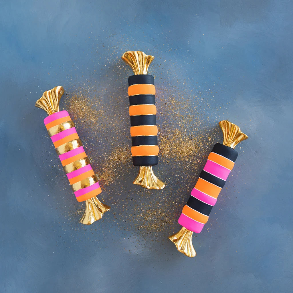 Glitterville Halloween taffy display set featuring three whimsical oversized wrapped candies in black, orange, hot pink, and metallic gold stripes with shimmering gold twisted ends.