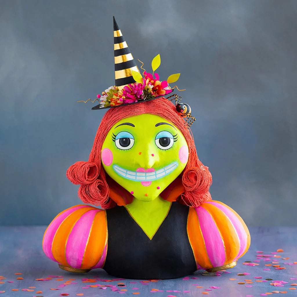 Glitterville Itchy Witchy Bust display Halloween decoration featuring a whimsical lime-green witch with bright red curled hair, a black and gold striped pointed hat decorated with colorful flowers, pink and orange striped sleeves, and a playful spooky smile.
