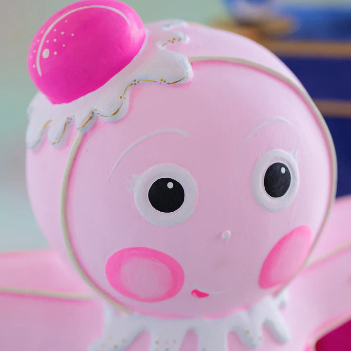 Close-up of the Glitterville Light Pink Dippsy gingerbread figure featuring a soft pink face, expressive white icing eyes and brows, rosy pink cheeks, a delicate smile, and a bright pink gumdrop headpiece with white icing and gold accents.