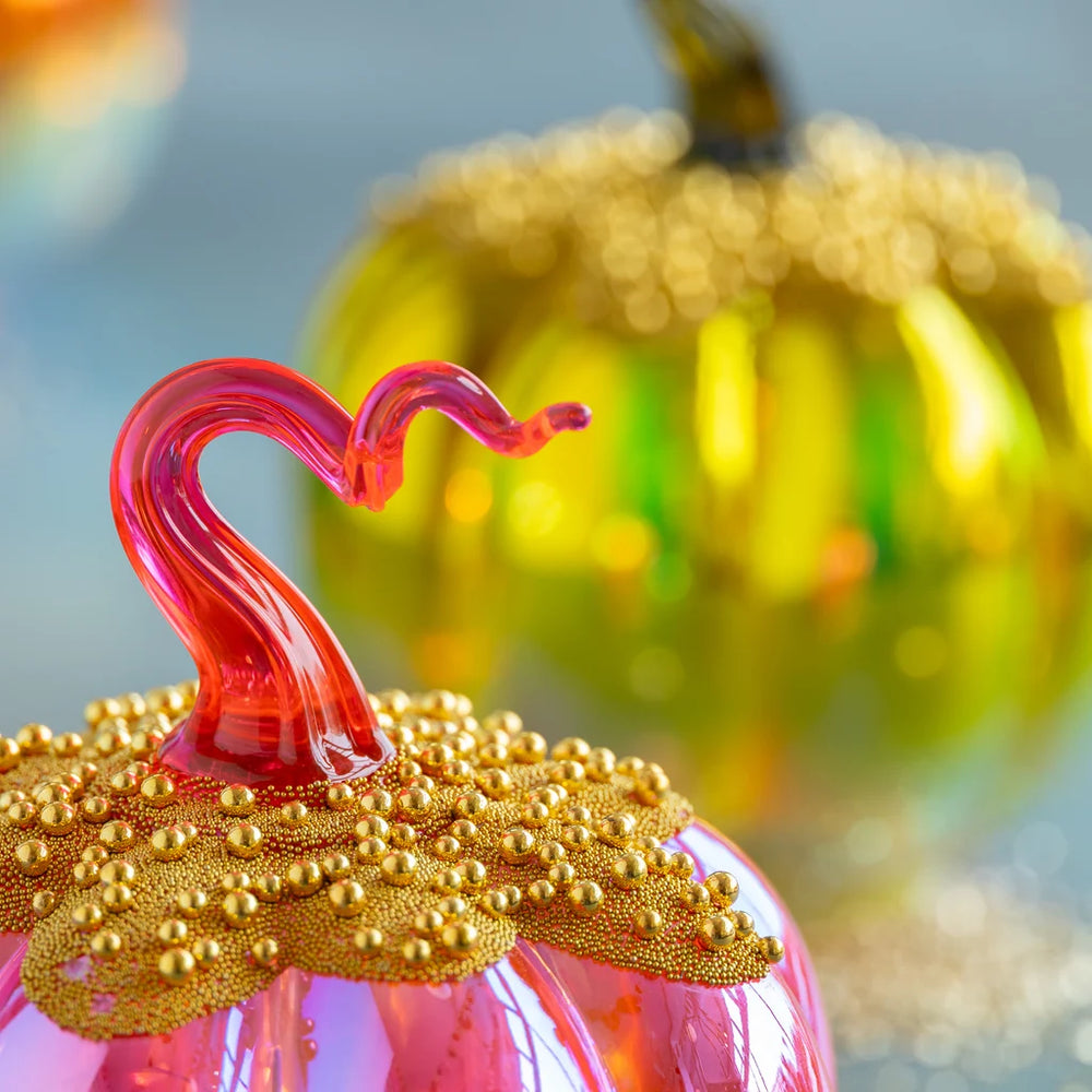 Close up on Glitterville's pink lighted pave pumpkin stem complete with two different sizes of gold beads on top of the pumpkin body itself. Blurred in the background, the green pumpkin can be seen.