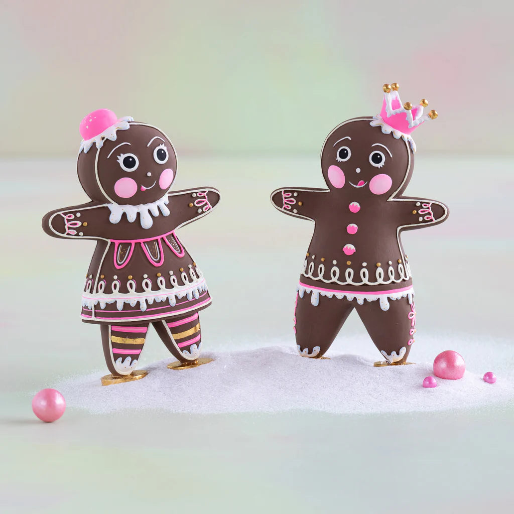 Glitterville Brand Mini Dippsy and Dough gingerbread figures with brown bodies, pink and white icing details, gold accents, and pink headpieces, displayed together on a snowy surface.