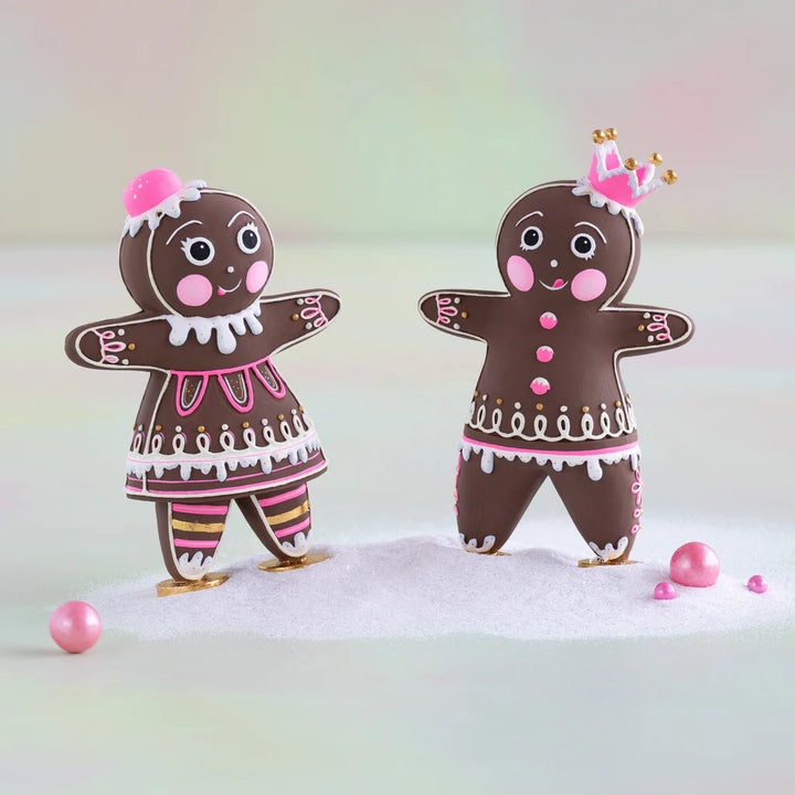 Glitterville Brand Mini Dippsy and Dough gingerbread figures with brown bodies, pink and white icing details, gold accents, and pink headpieces, displayed together on a snowy surface.