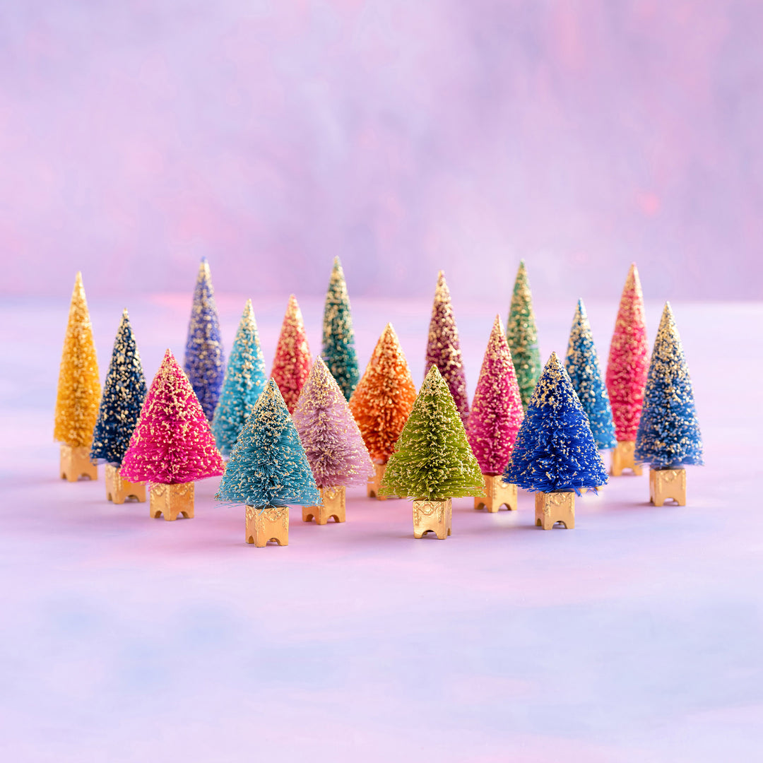 Glitterville Gilded French Forest bottle brush tree set featuring assorted colorful bottle brush trees with gold bases, displayed against a soft pink winter backdrop.