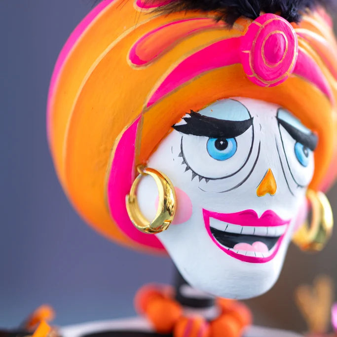 Glitterville Nelly Skelly Fortune Telly close-up showcasing the hand-painted skeleton face, bright blue eyes, pink lips, orange turban-style hair, gold hoop earrings, and detailed painted features.