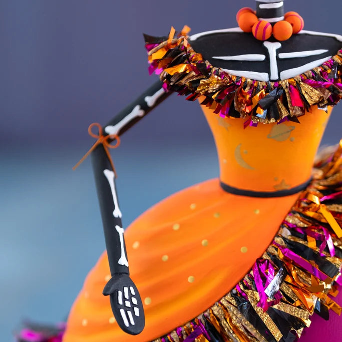 Glitterville Nelly Skelly Fortune Telly close-up showcasing the hand-painted orange bodice, black-and-white skeleton chest and neck, articulated arm, gold painted details, and colorful metallic fringe trim.