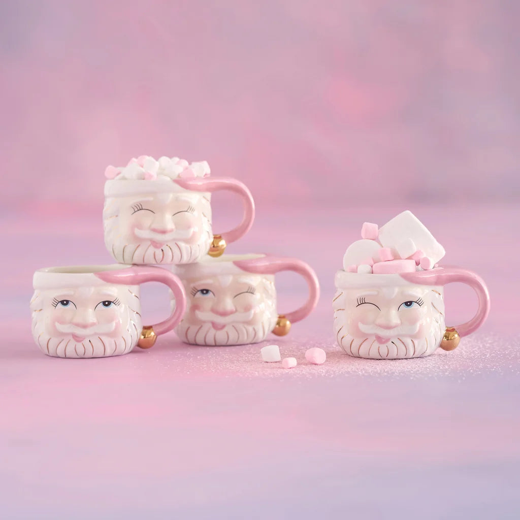 Glitterville Papa Noel pink Santa mug set featuring four ceramic Santa Claus mugs with pink hats, gold accents, different facial expressions, and pink and white marshmallow toppings.