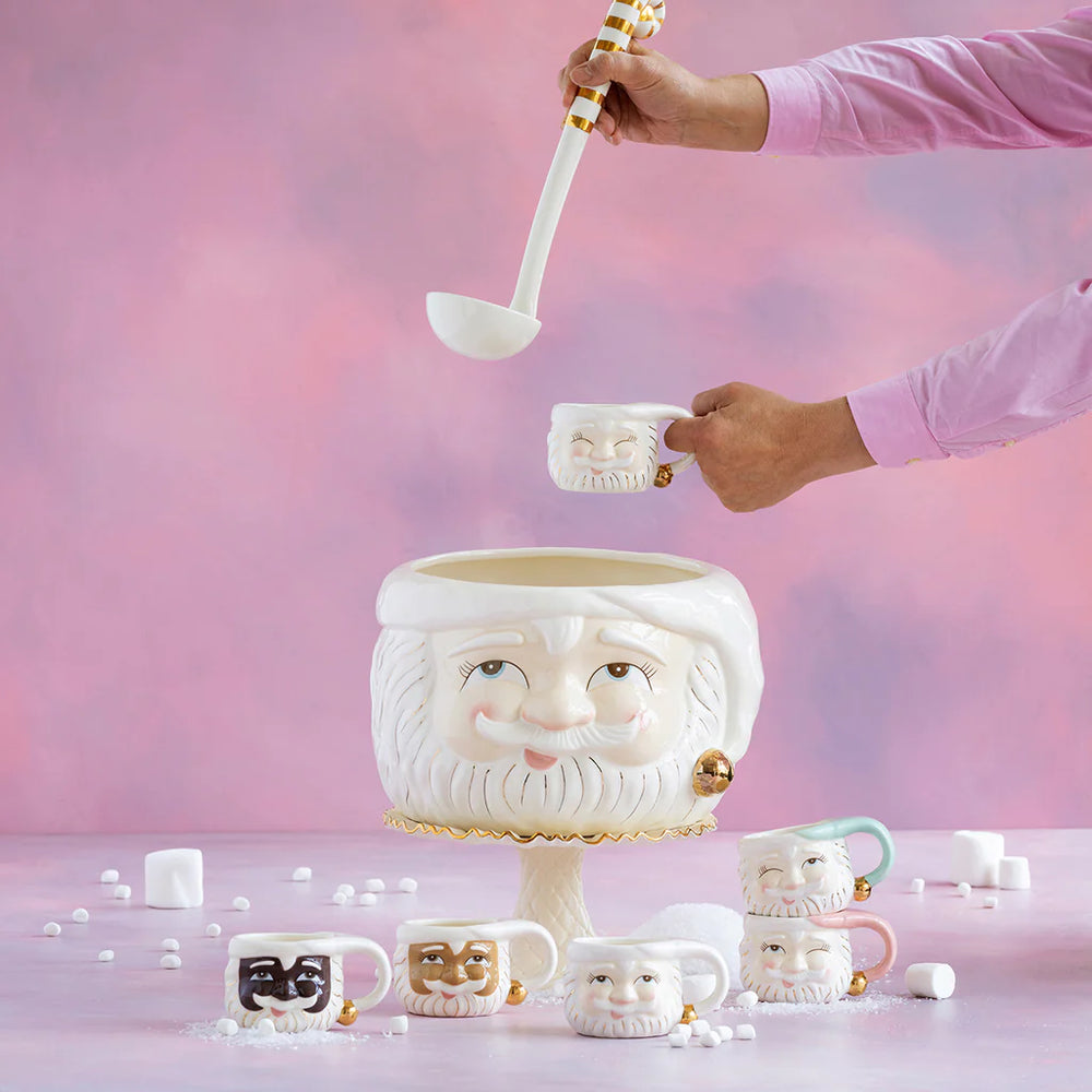 Glitterville Papa Noel Santa punch bowl set with matching mini Santa face mugs, showing punch being served into a mug with additional white, pink, brown, and black Santa mug options displayed around the bowl.