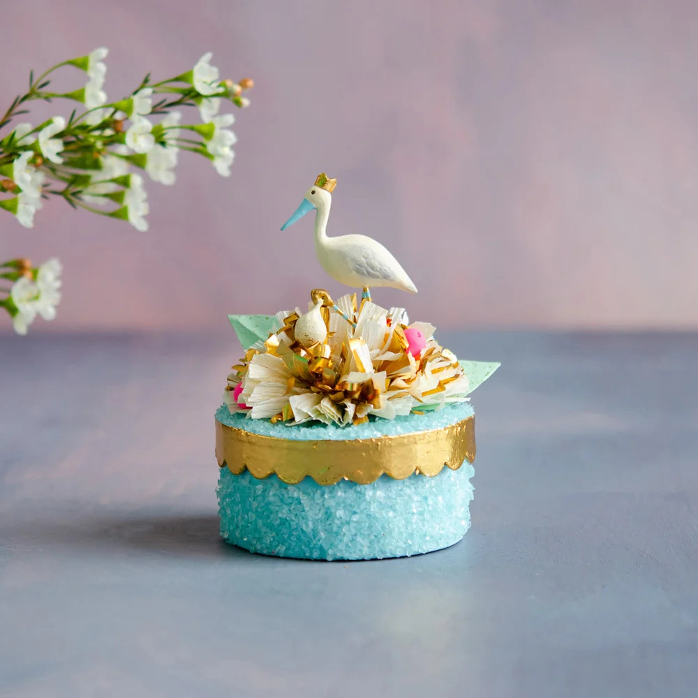 Glitterville Paper Mache Blue Royal Stork Favor Box featuring a textured blue box with gold trim, floral accents, and a small crowned stork topper.